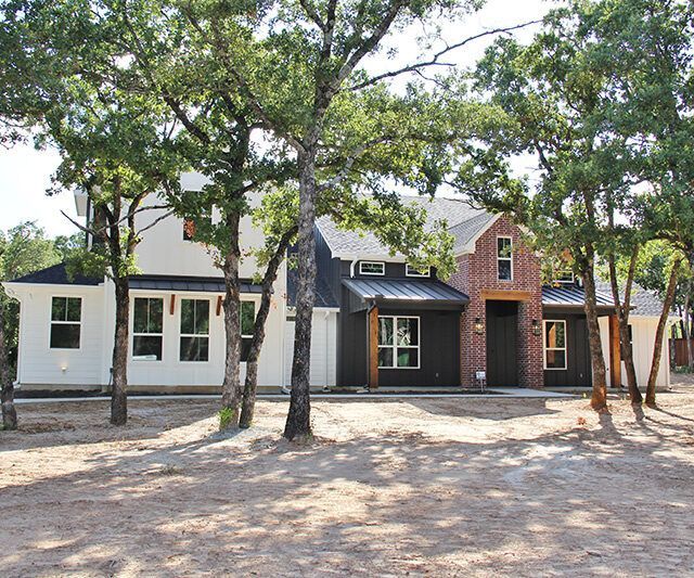 A white house with a black roof is surrounded by trees