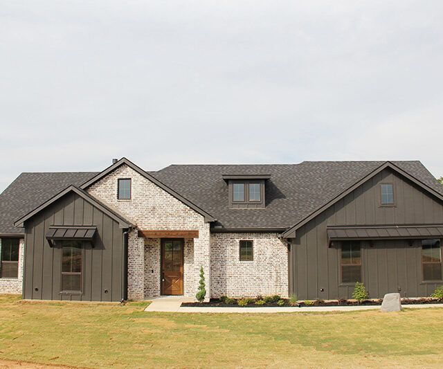 A large brick house with a black roof is sitting on top of a lush green field.
