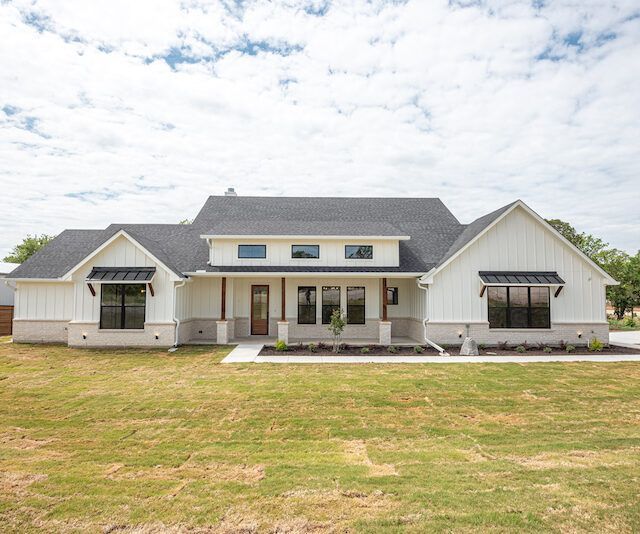A white house with a black roof is sitting on top of a lush green field.