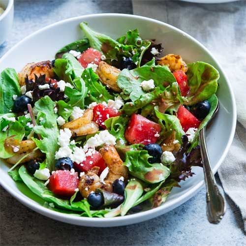 Salad with watermelon, blueberries, feta cheese, and lettuce in a white bowl.