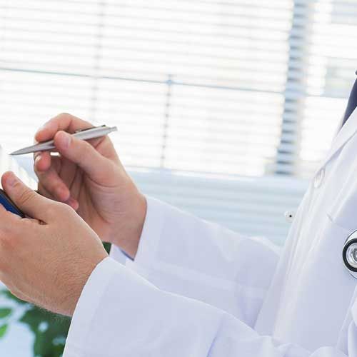 Doctor in white coat holding pen and small device near a window.