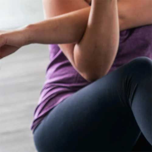 Person in purple shirt and dark leggings, arms crossed, seated.