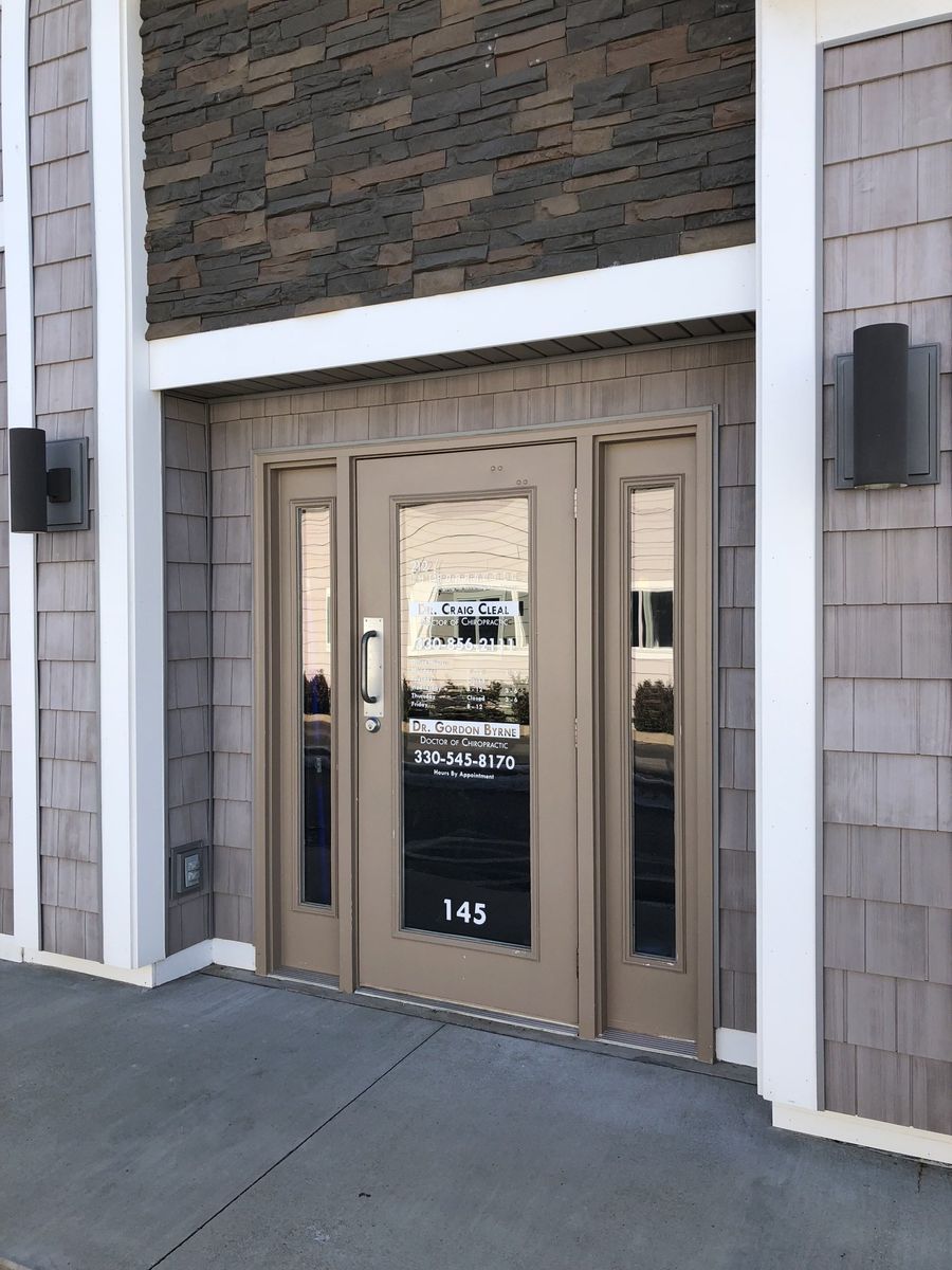 Tan door with glass panels and sidelights, building address 145, flanked by gray shingle siding, and white trim.
