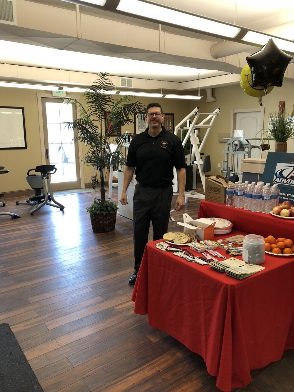 Man standing by a table with food in a physical therapy office. Balloons and equipment are visible in the background.