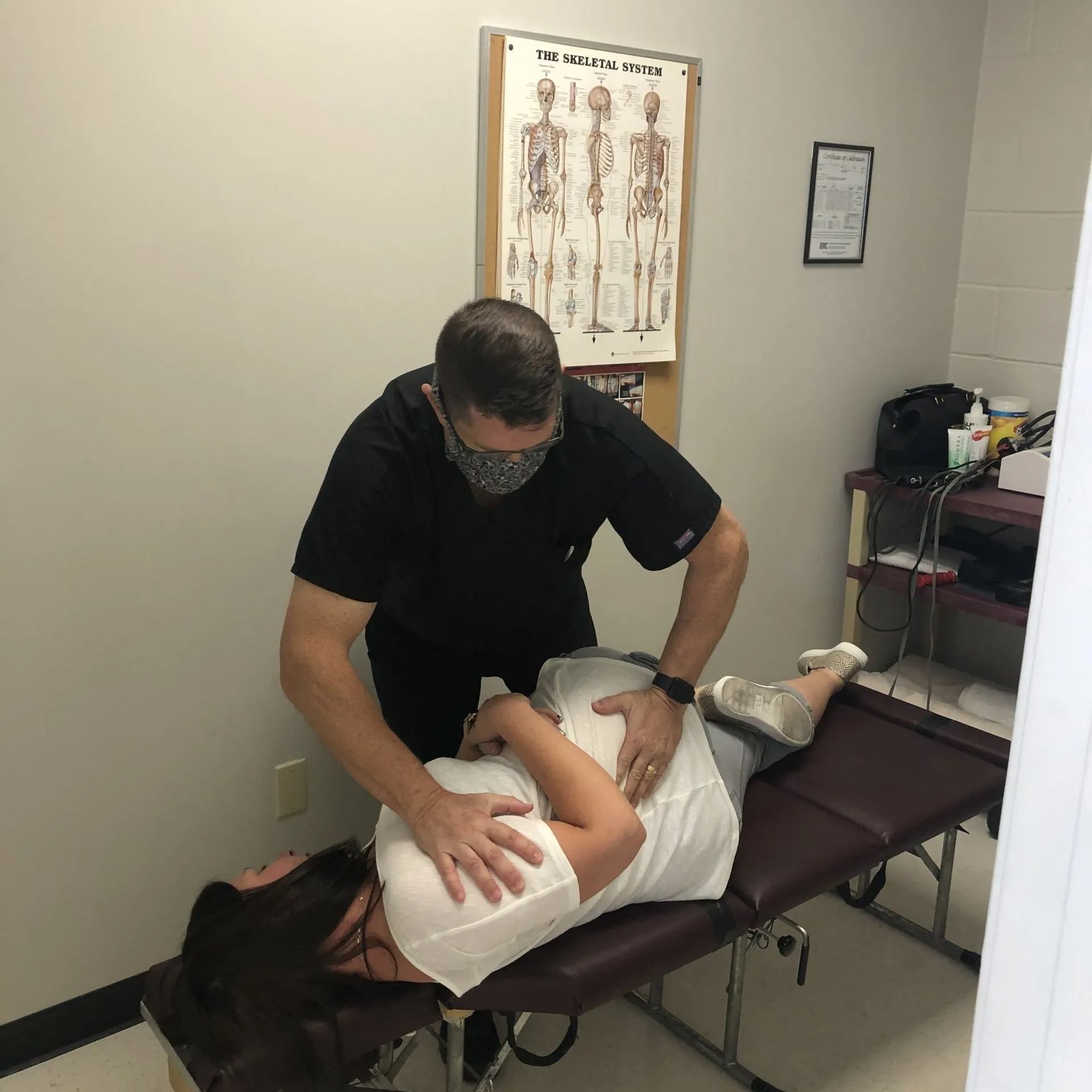 A person receiving chiropractic care on a table by a masked healthcare provider in an office setting.