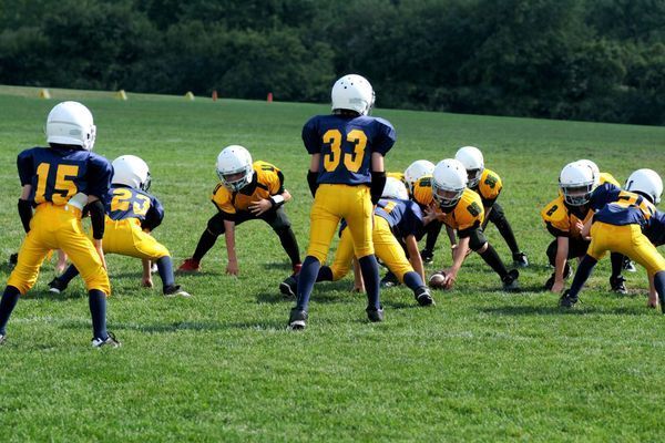 Youth football players in blue and yellow uniforms huddle on a grassy field.