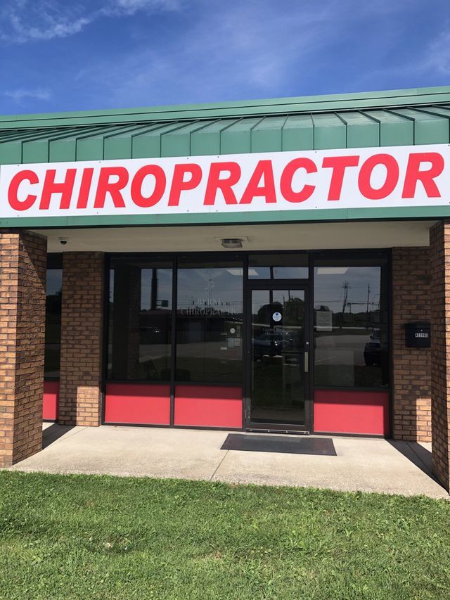 Chiropractor office building with red sign, glass door, and green roof under a blue sky.