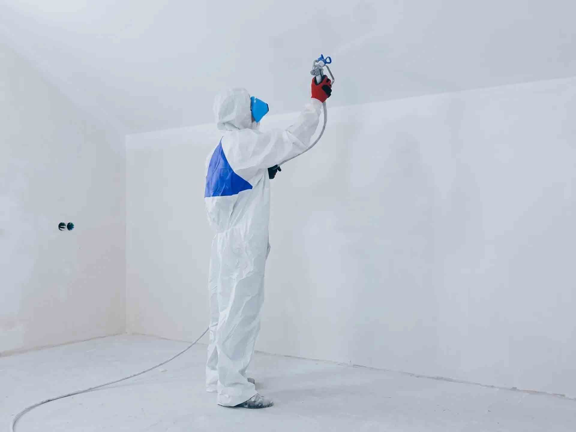 Une personne en combinaison de protection blanche peint à la bombe une pièce blanche avec un pistolet à peinture rouge.