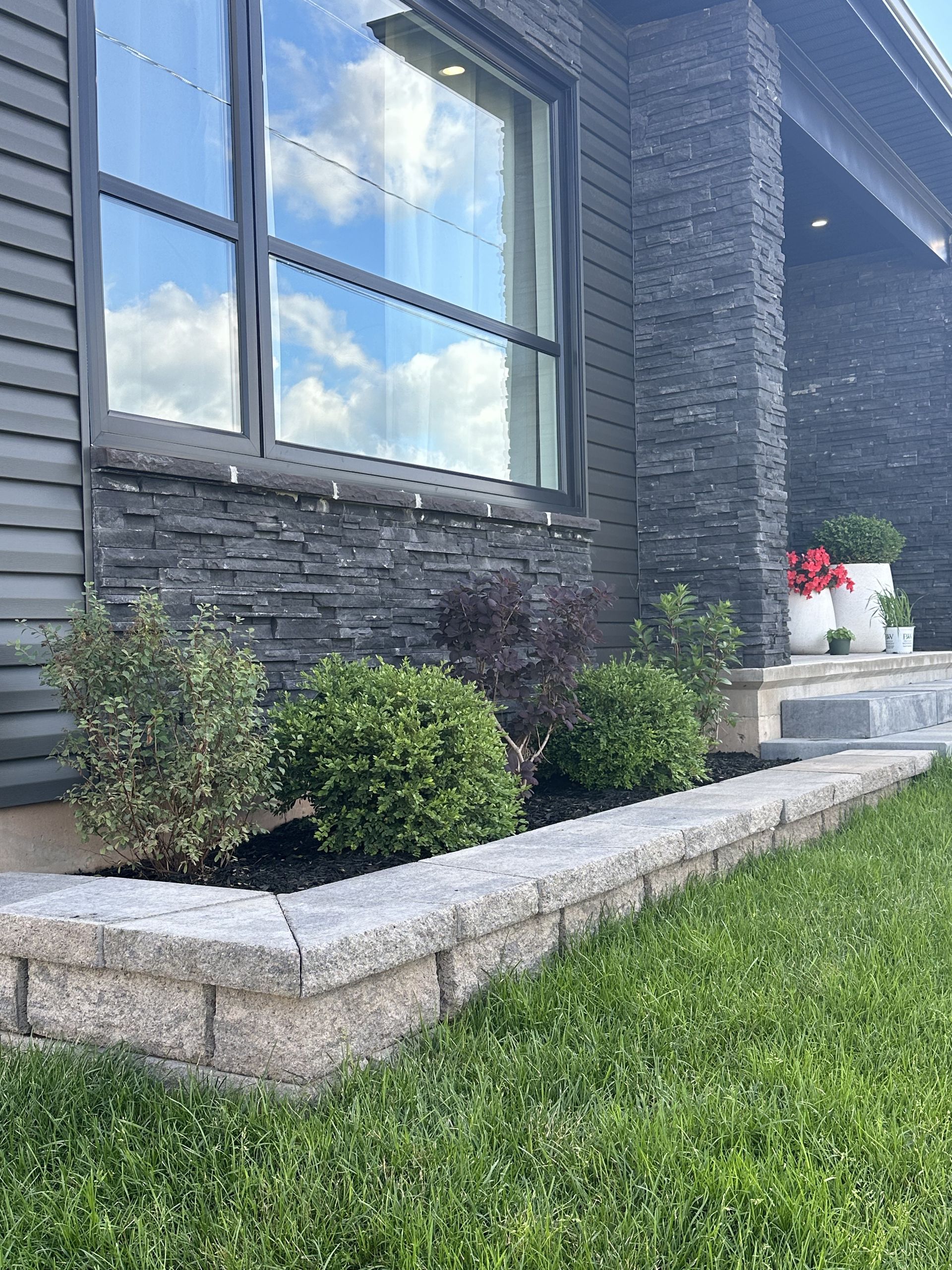 A house with a stone wall and a planter in front of it.