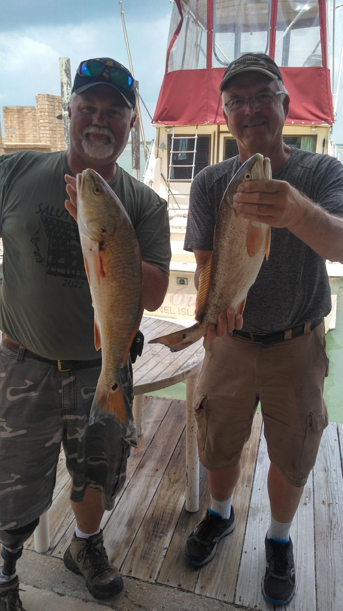Two men holding up redfish on a dock, one man with a prosthetic leg.