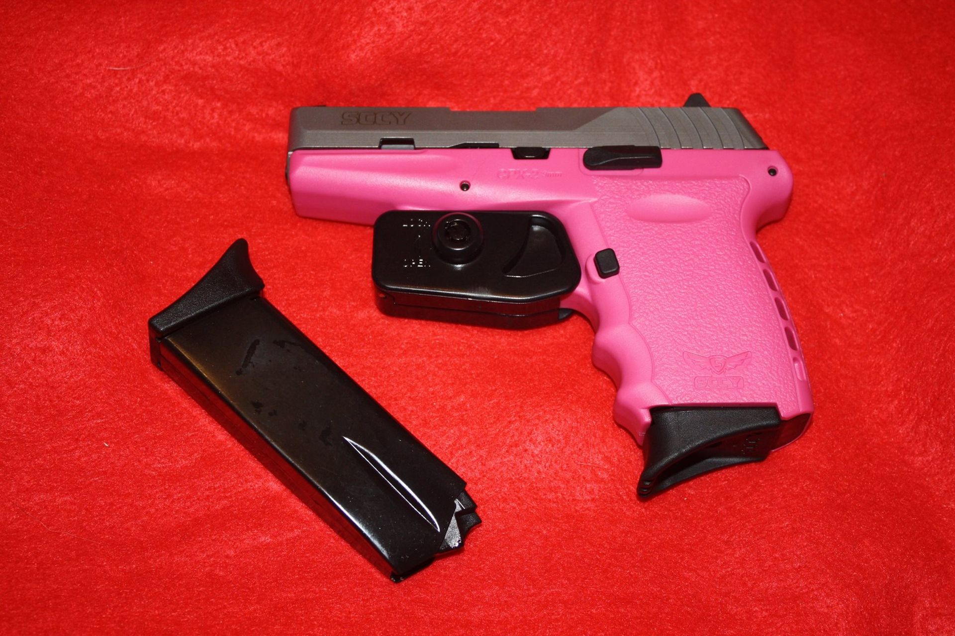 Pink handgun with a black magazine on a red surface.