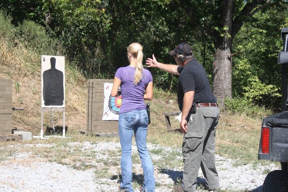 Woman receiving shooting instruction at an outdoor range, with instructor pointing at target.