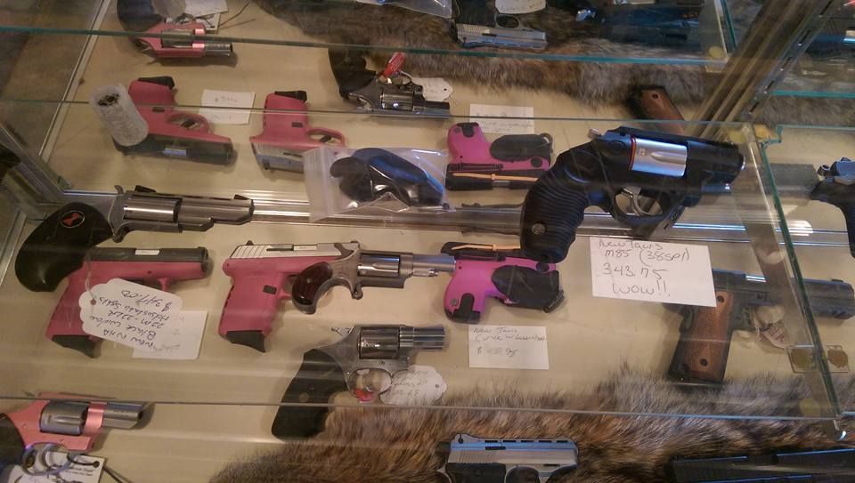 Guns on display in a glass case, many with pink grips.