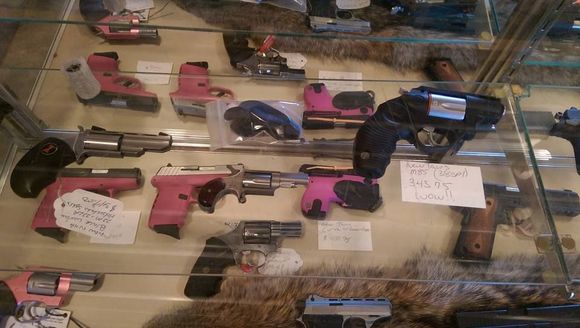 Display case with various handguns, some with pink accents, in a gun store.