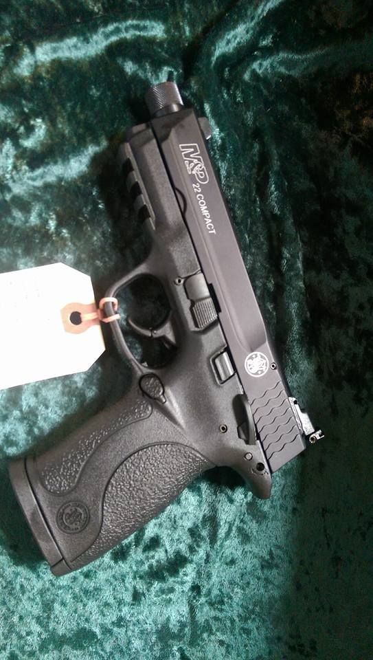 Black Smith & Wesson M&P pistol with a white tag, angled against a teal background.