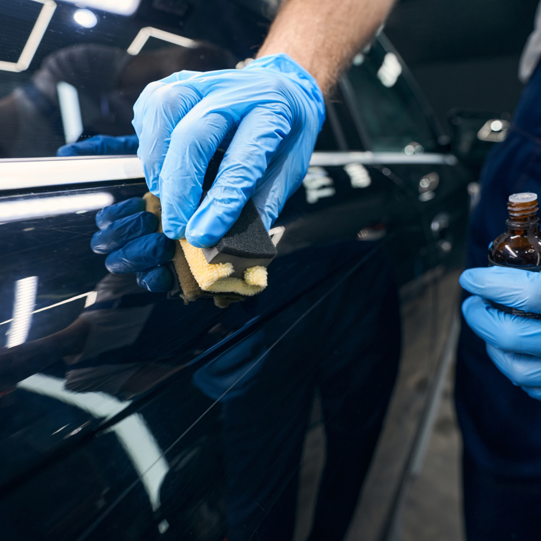 A person wearing blue gloves is cleaning a car with a sponge.