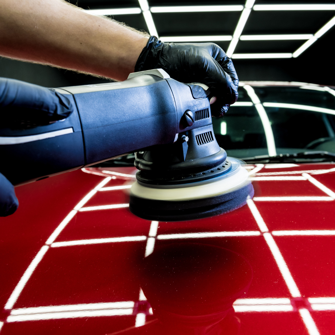 A person is polishing a red car with a machine