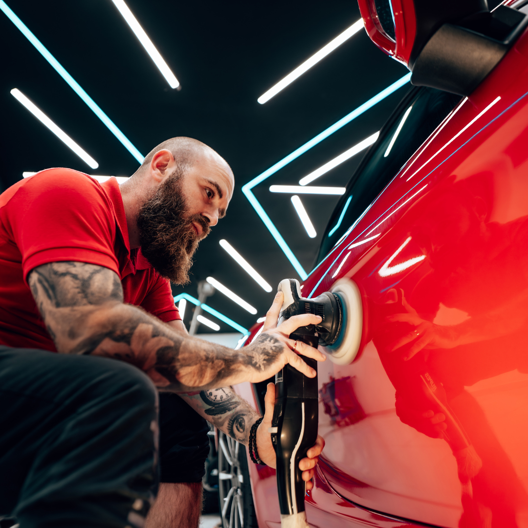 A man is polishing a red car with a polisher.