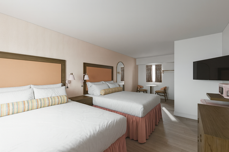 Two beds in a hotel room with peach headboards and light pink bedskirts.