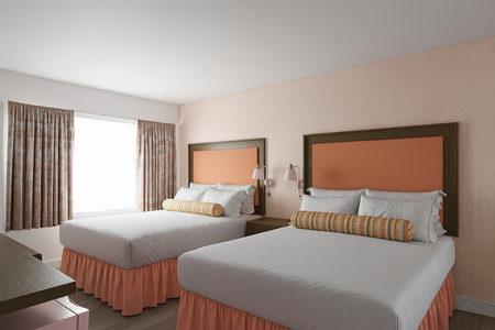 Hotel room with two double beds, peach-colored headboards and bed skirts, a window with curtains.