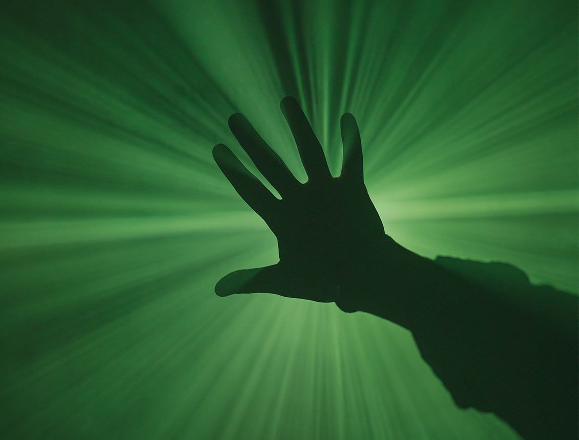 close up silhouetted open hand in front of a green light background