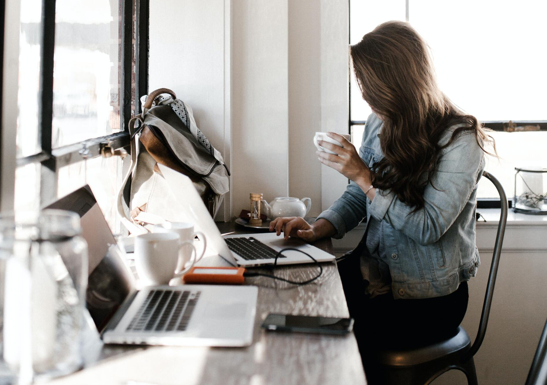 Photo of woman working at laptop holding coffee writing social media copy