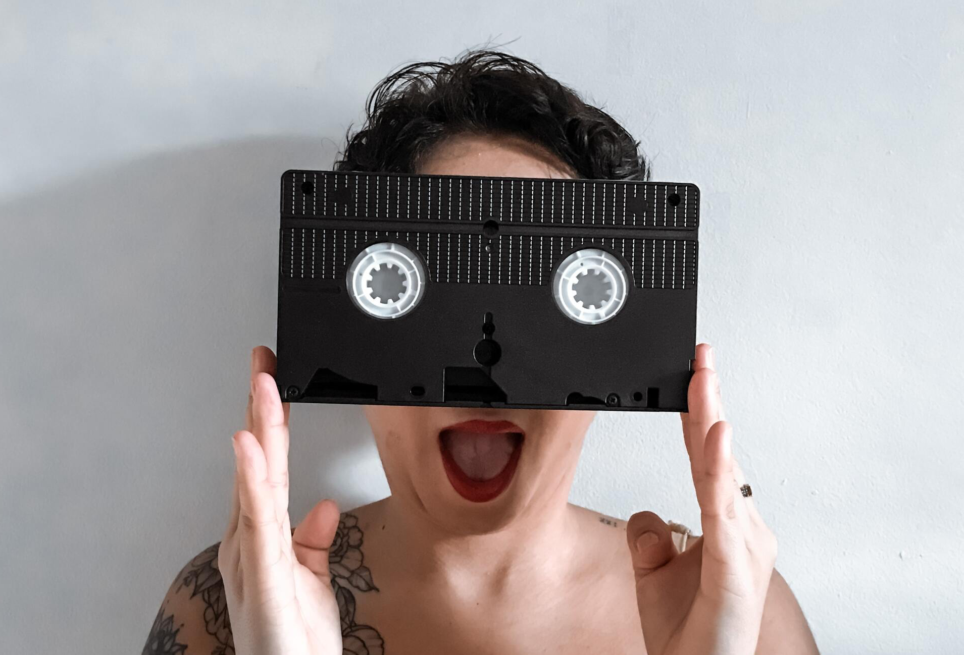 woman with surprise expression holding a vhs tape in front of her face