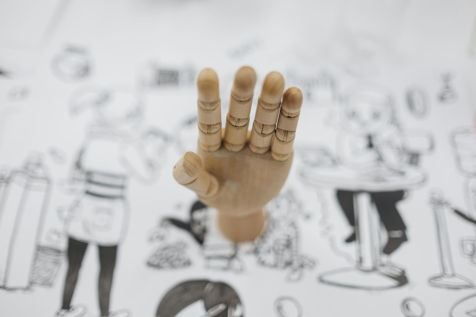 Wooden hand model displaying four fingers on a table with a black and white illustrated design.