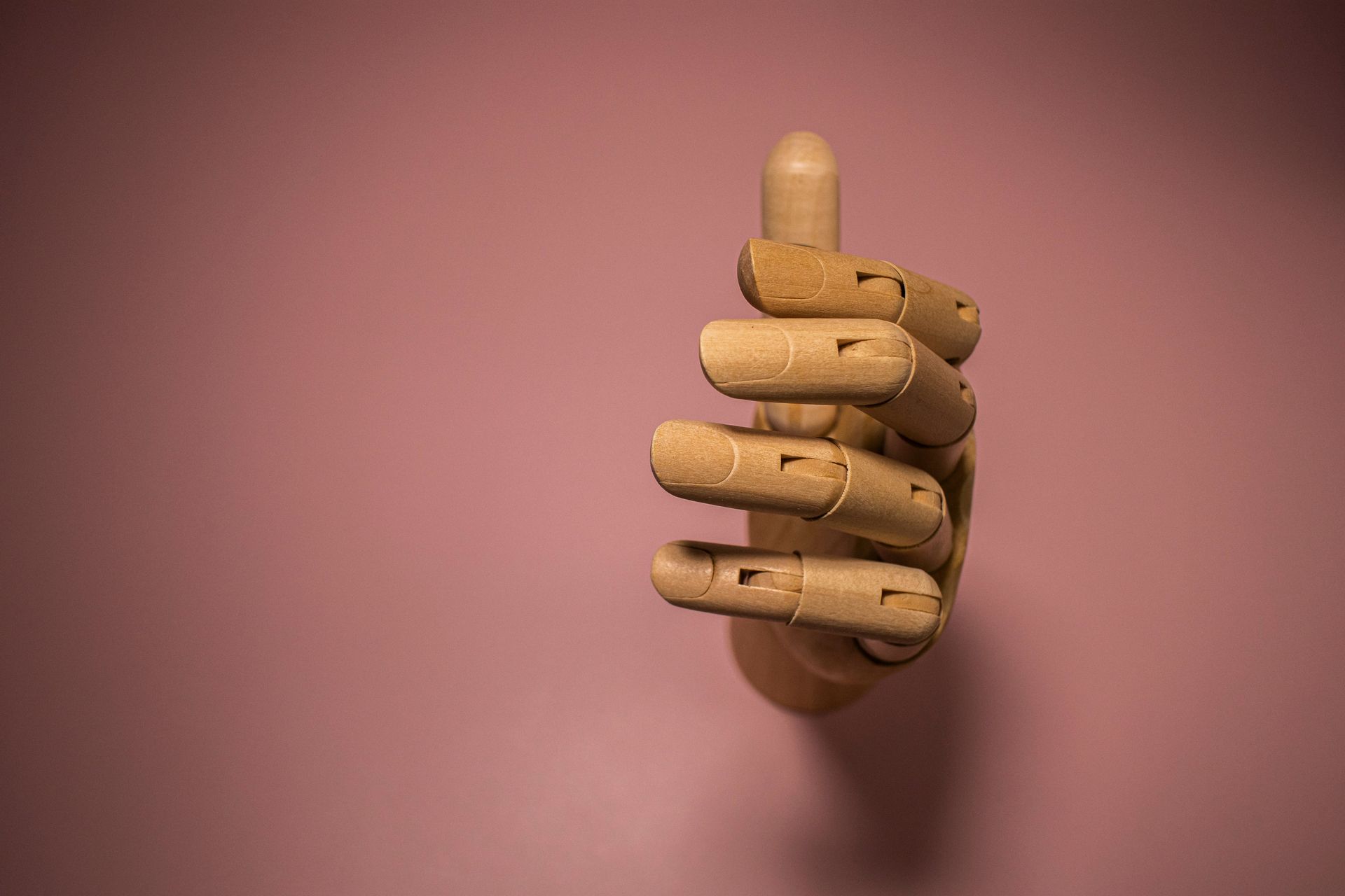Wooden articulated hand giving a thumbs-up against a pink background.