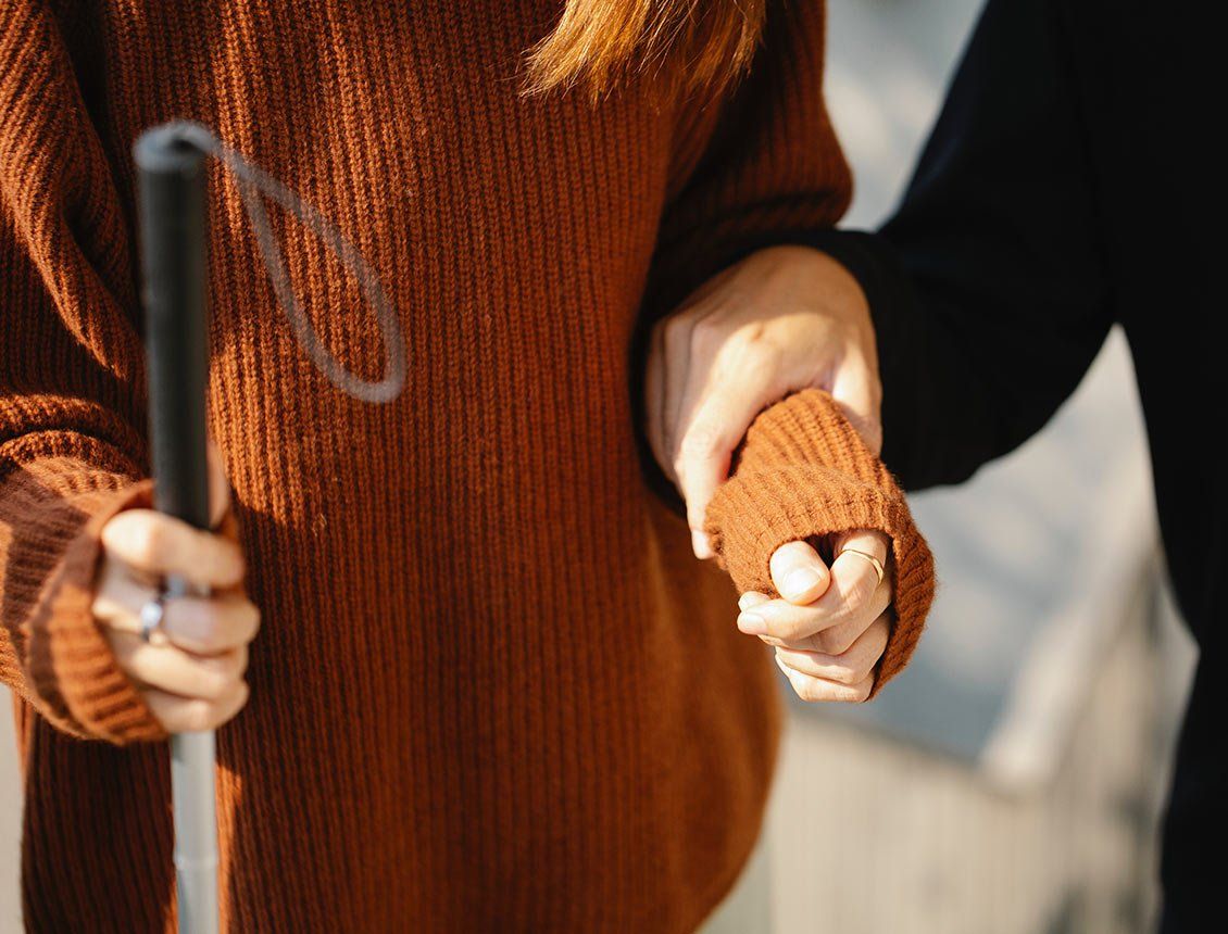 Close up image of a person's hand holding another persons' hand who is blind walking with a blind person's pole