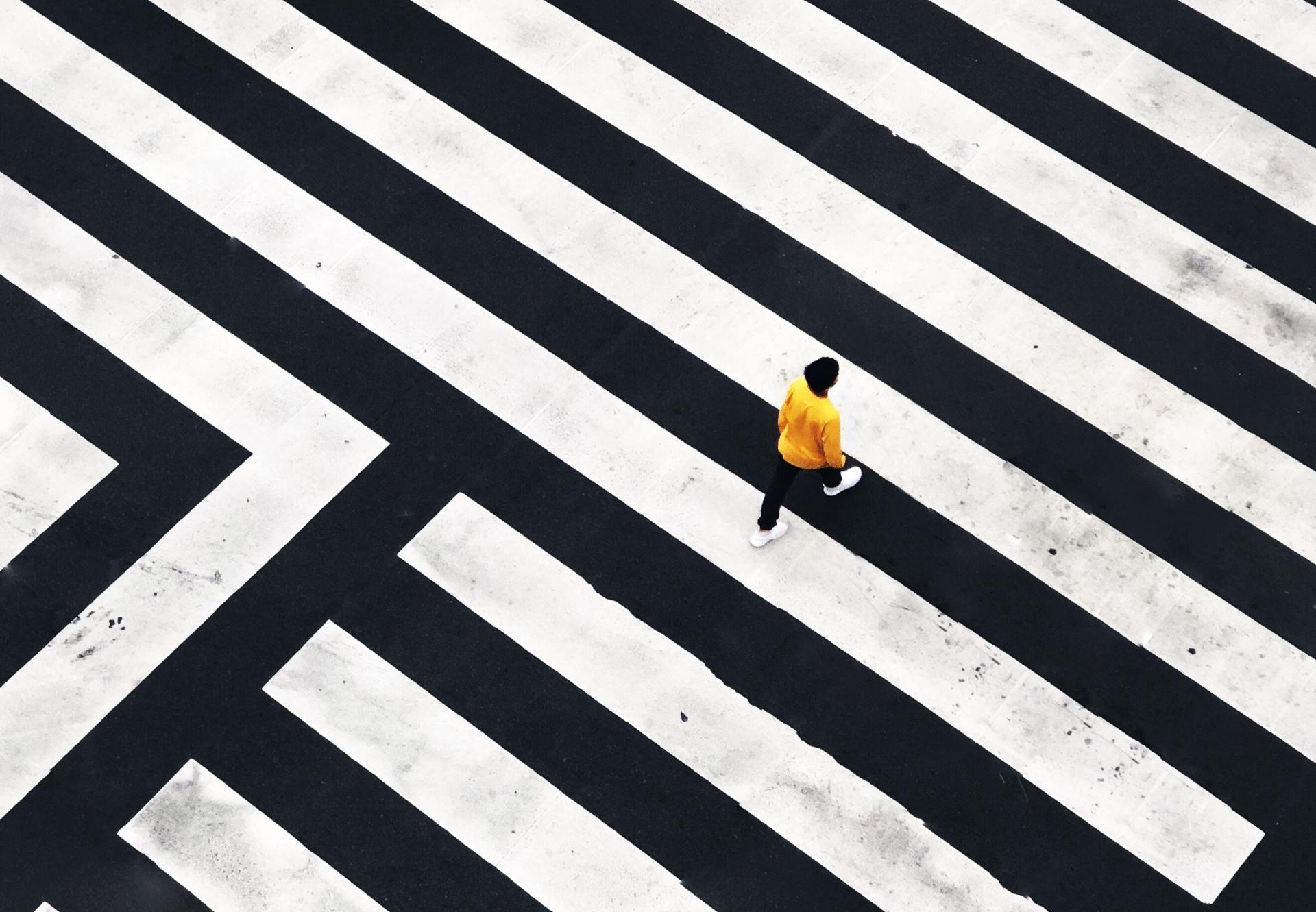 Image of black and white lines on a street with a person in yellow walking through frame