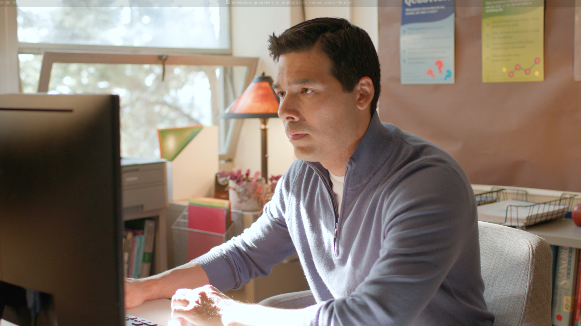 A woman wearing glasses is smiling while sitting in front of a laptop computer.