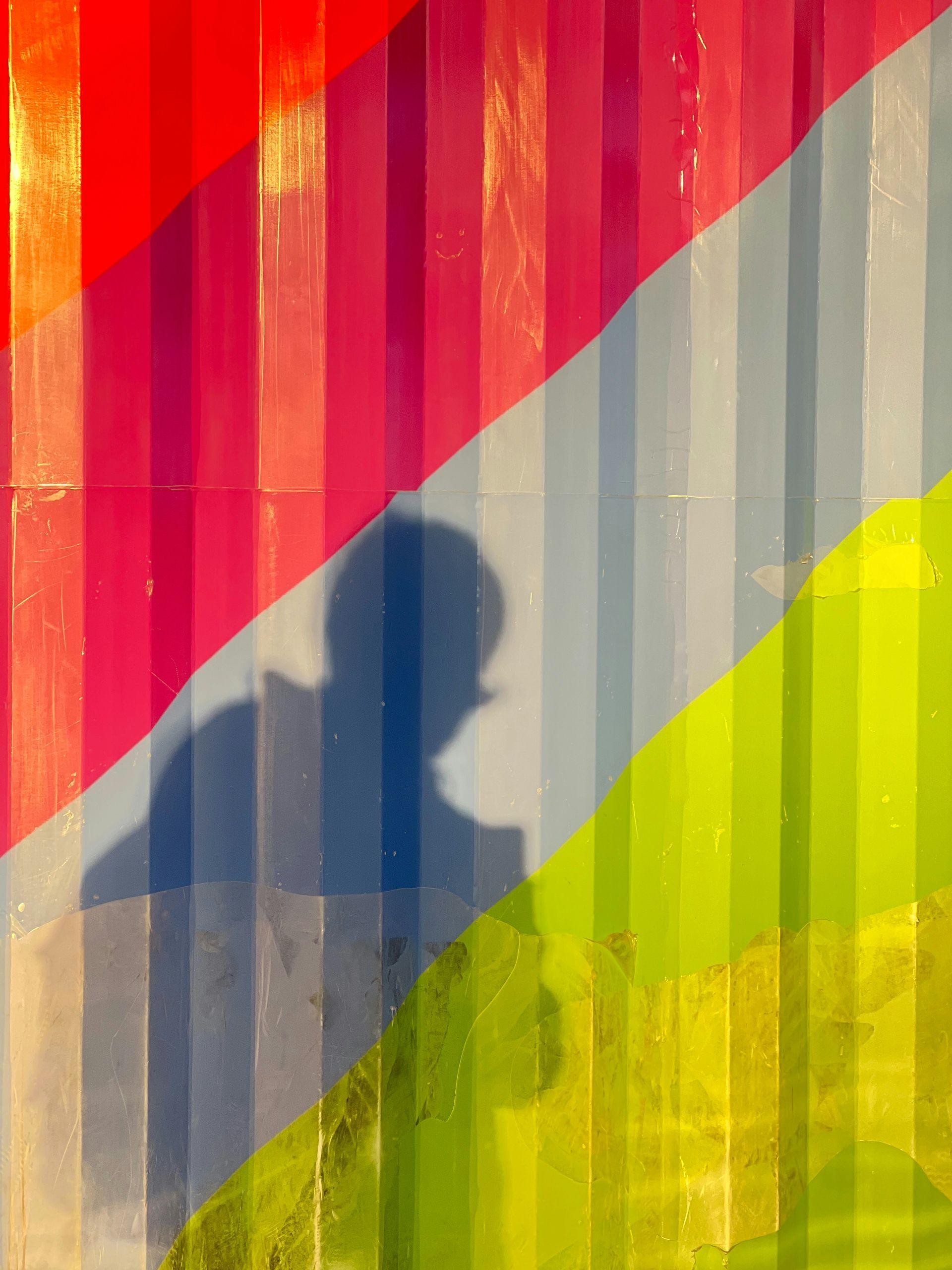 Shadow of person on colorful striped wall: red, pink, blue, green, and yellow stripes.