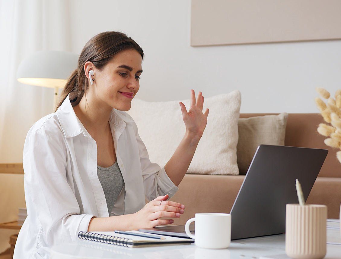 Image of woman slightly smiling and looking into laptop raising her hand