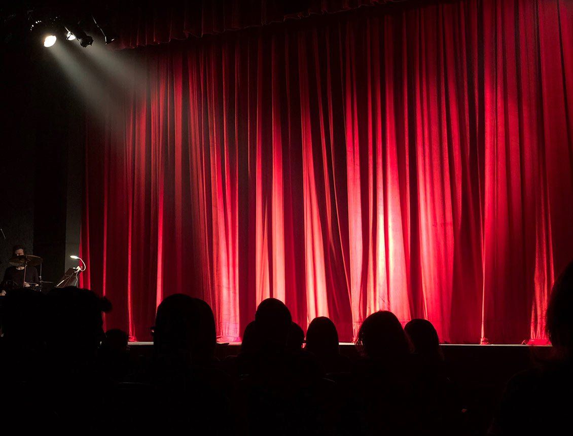 red theater curtain with lights shining on it with audience watching