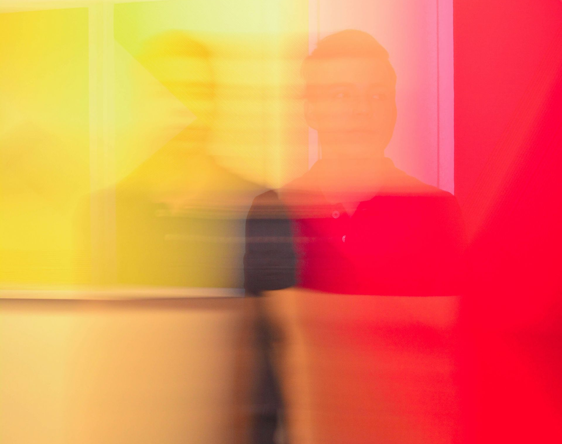 Blurred figure in front of a yellow painting with a large red shape on the right. Blurred figure in front of a yellow painting with a large red shape on the right.