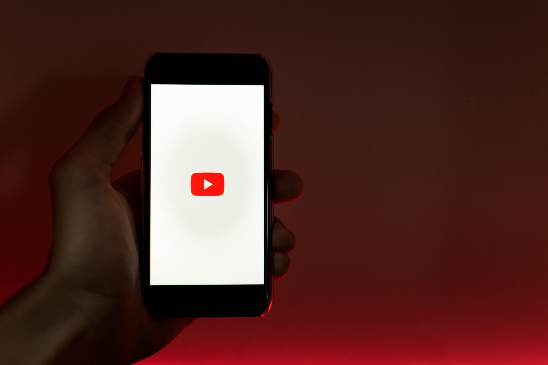 Hand holding phone in front of red background with youtube icon on phone screen