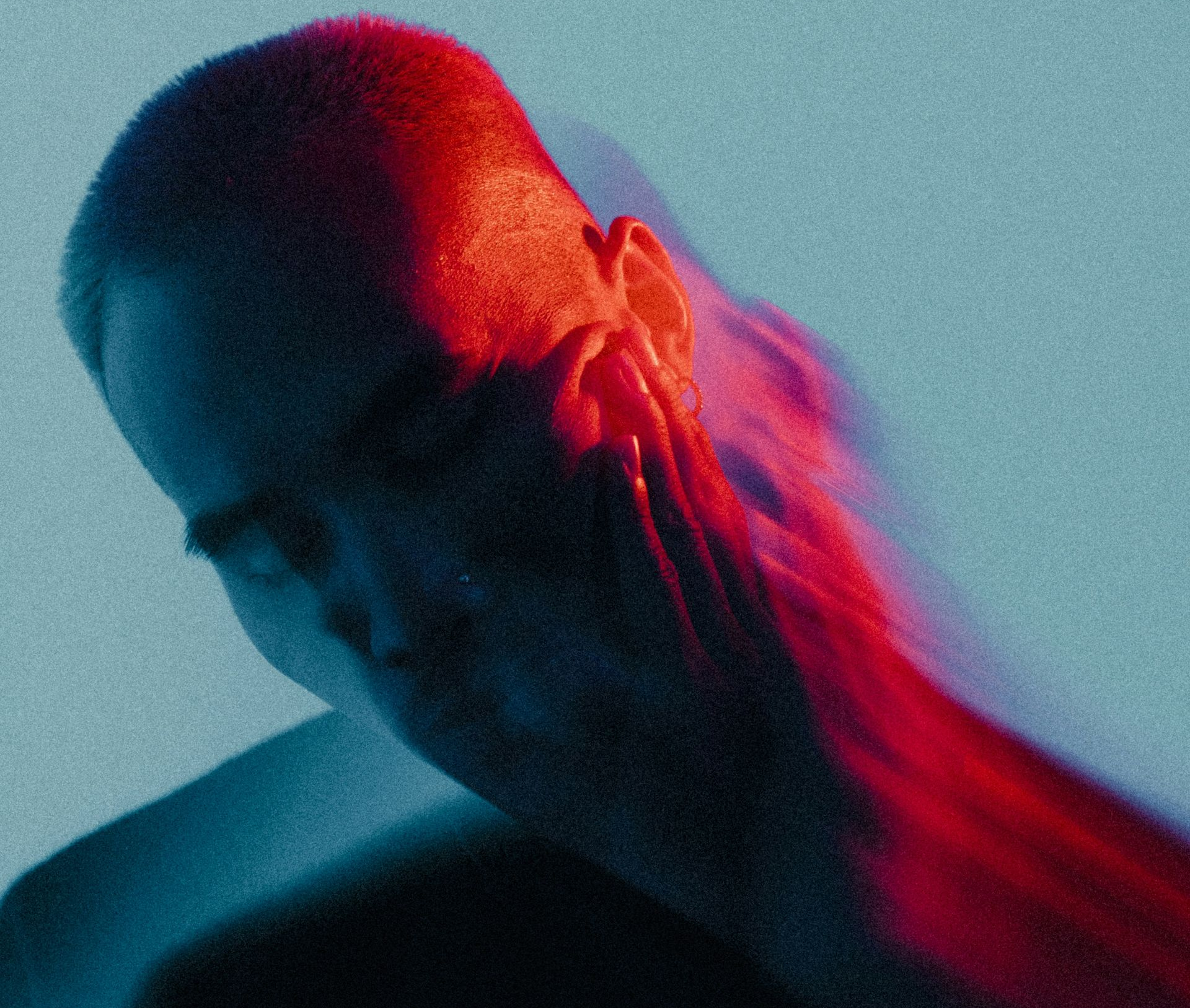 A person's head and shoulder illuminated by red and blue light, with a blurred silhouette. A person's head and shoulder illuminated by red and blue light, with a blurred silhouette.