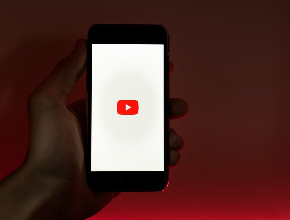 close up hand holding phone with youtube icon on screen with red lighted background