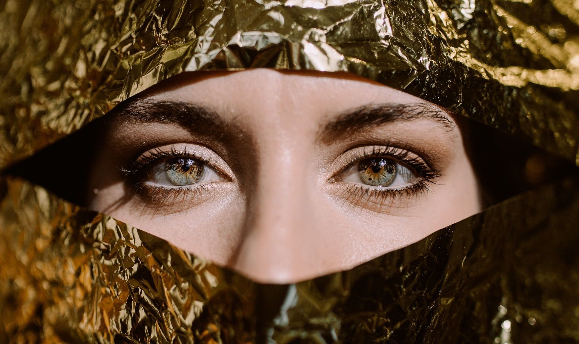 Closeup woman's eyes looking through gold tinfoil