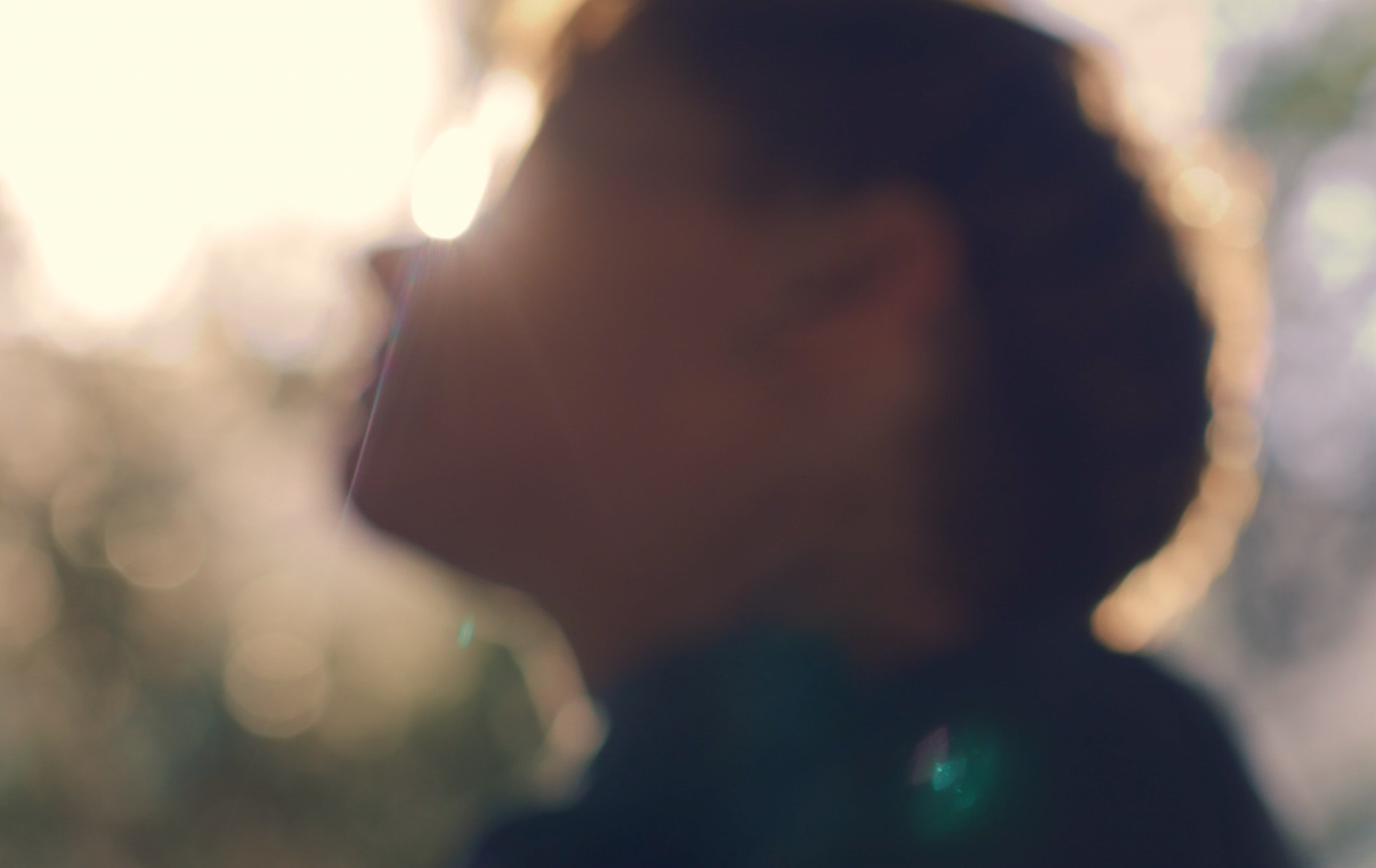 A close up of a person 's face with sun shining behind with a blurry background.