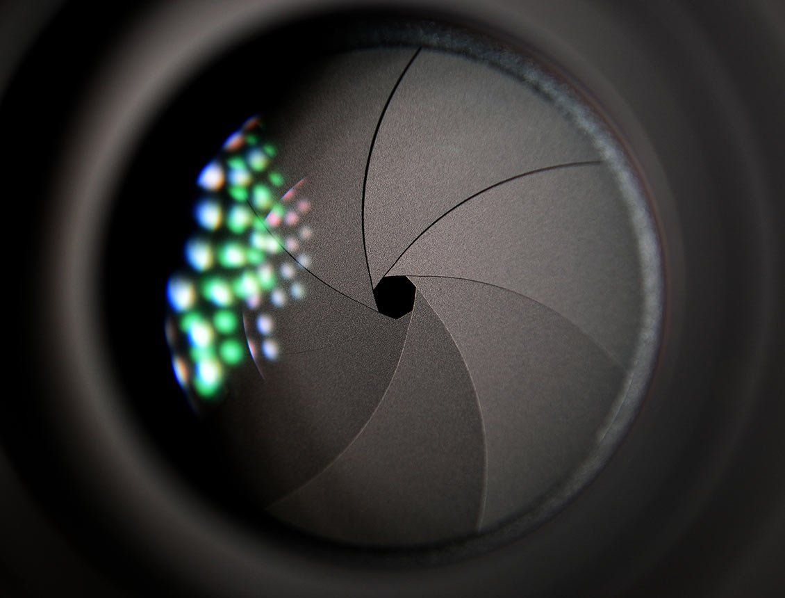 Image of a close up of a black camera aperture with colored light reflecting in lens