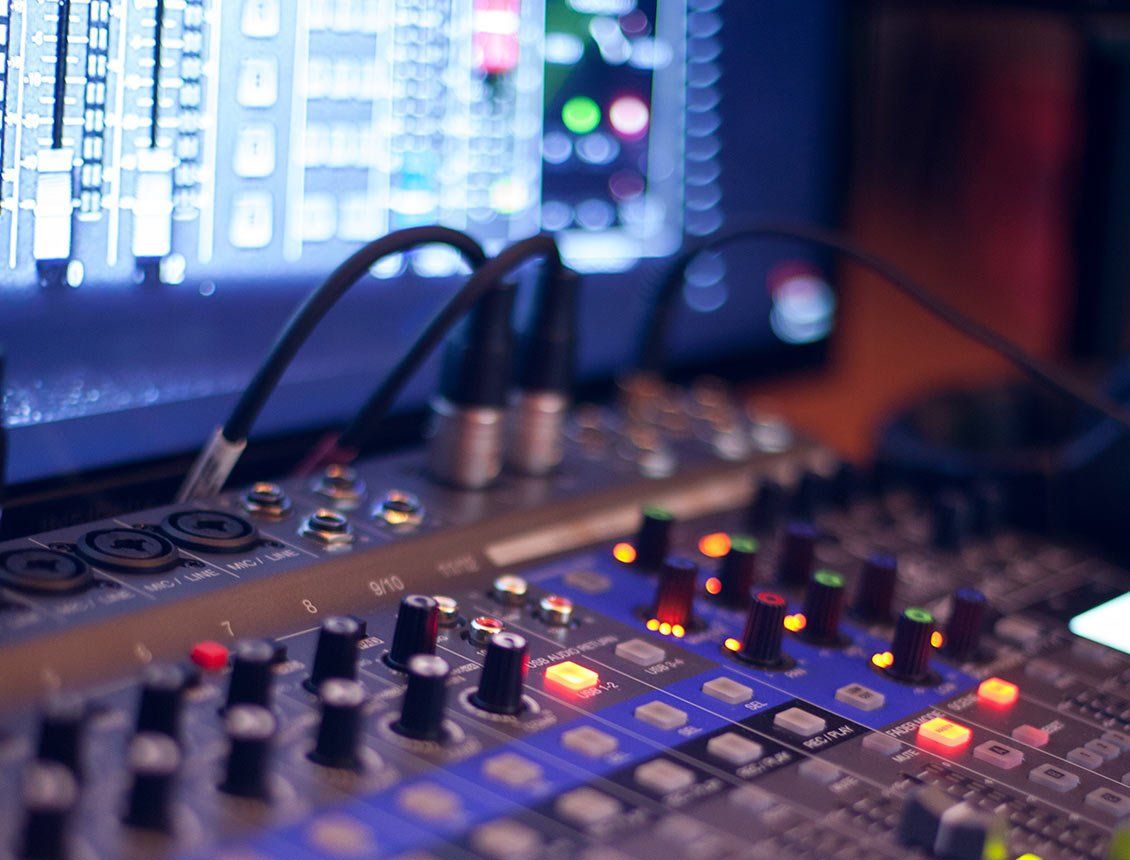 Close up image of audio mixing board with monitor in background