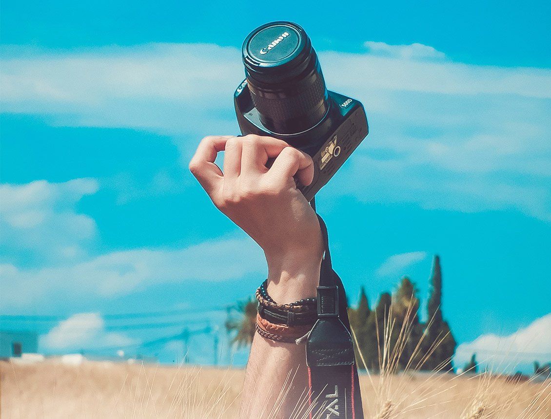 Close up hand holding up DSLR video camera in field with blue sky behind