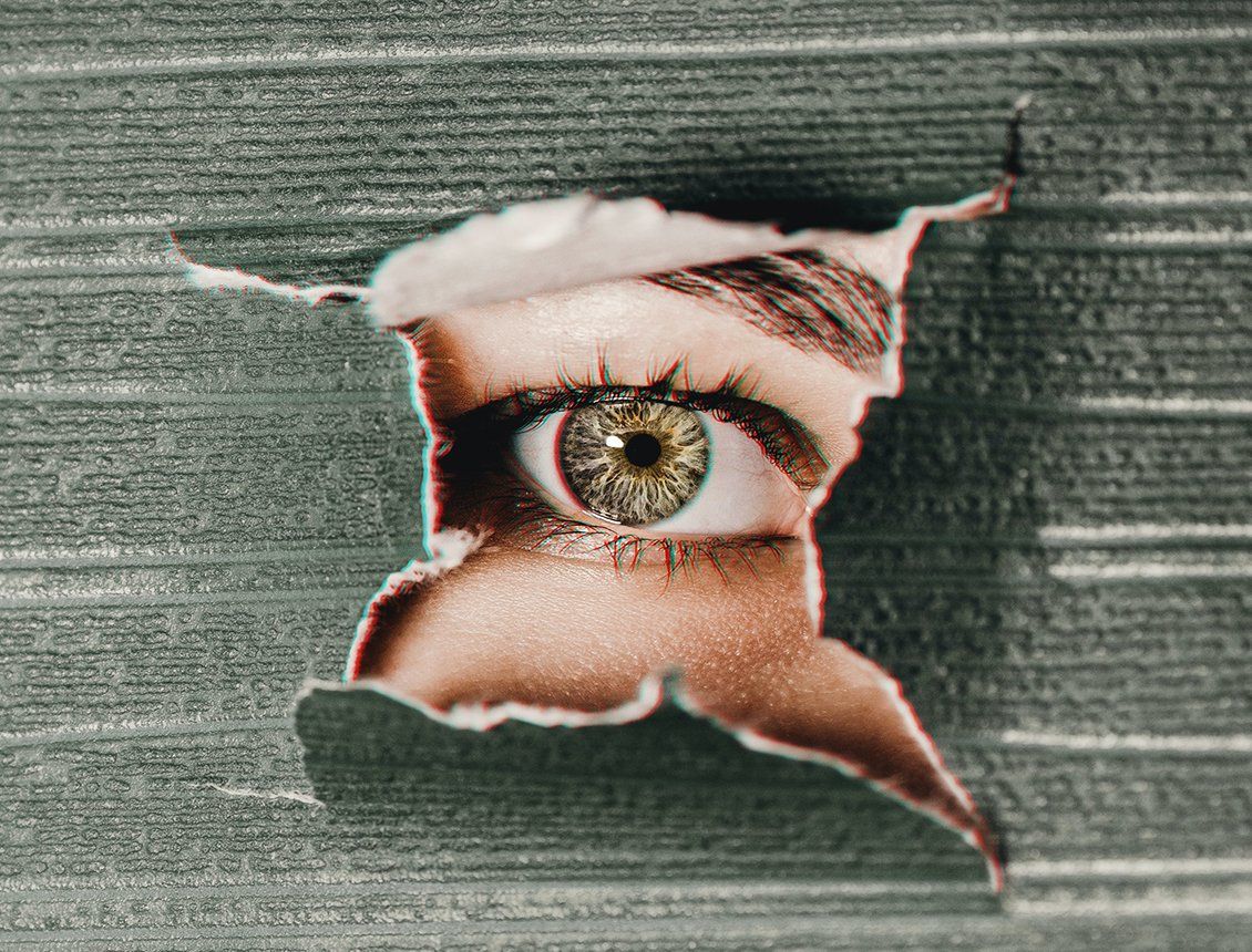 Image of a close up female eye looking through torn paper