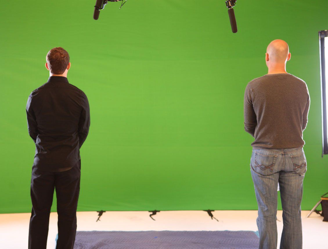 Behind the scenes photo from a Spin Creative video production shoot in Seattle, featuring two crew members standing in front of a large green screen background on a sound stage.