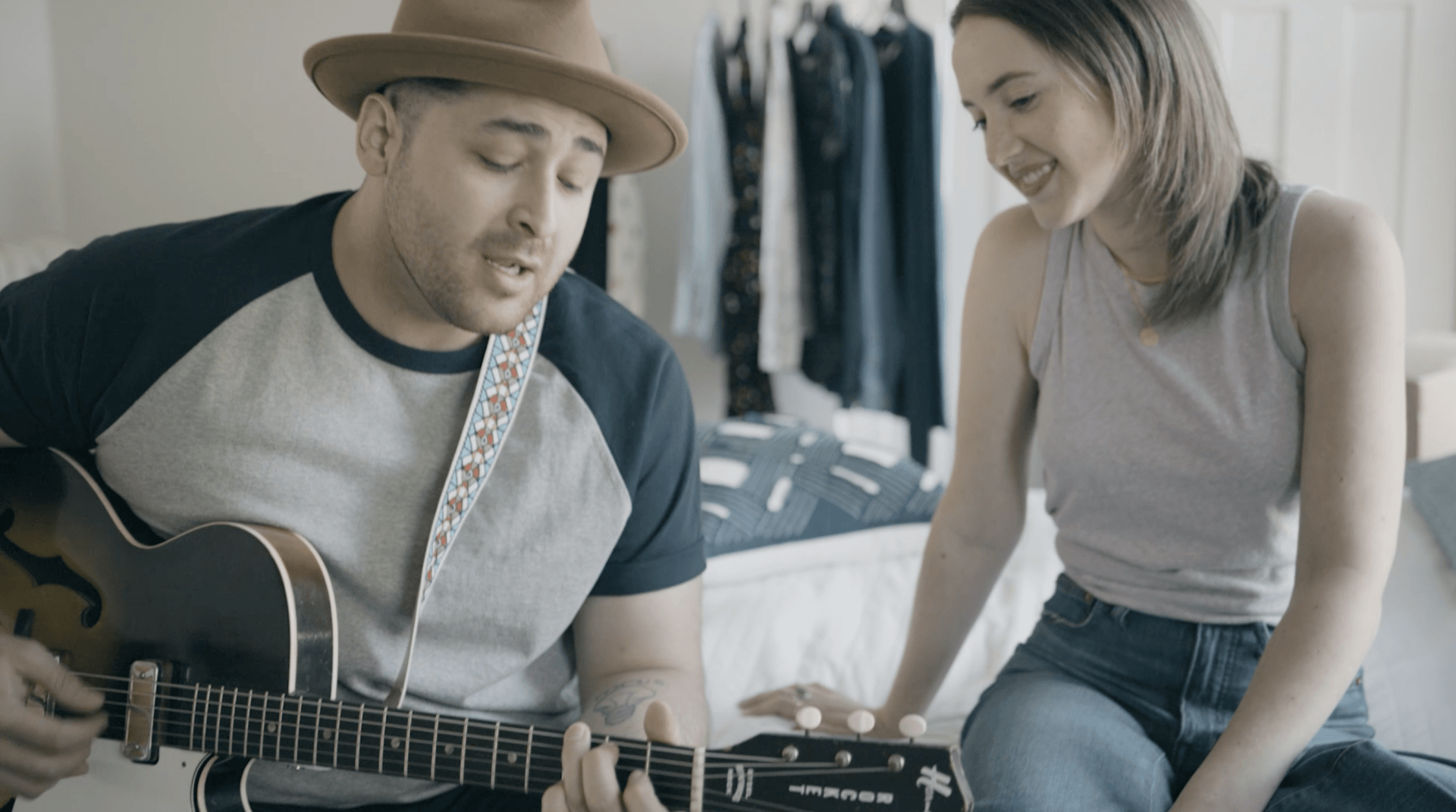 Man plays guitar in bedroom as girlfriend listens and looks at him playing