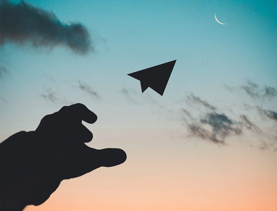 close up silhouetted hand throwing a paper airplane into sky with moon