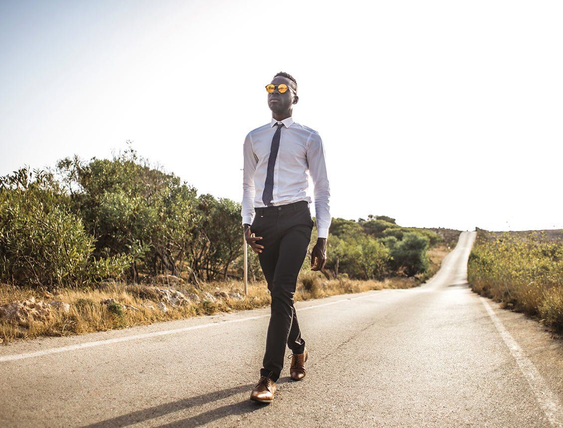 Image of man dressed in tie and slacks walking on empty road with mirrored sunglasses
