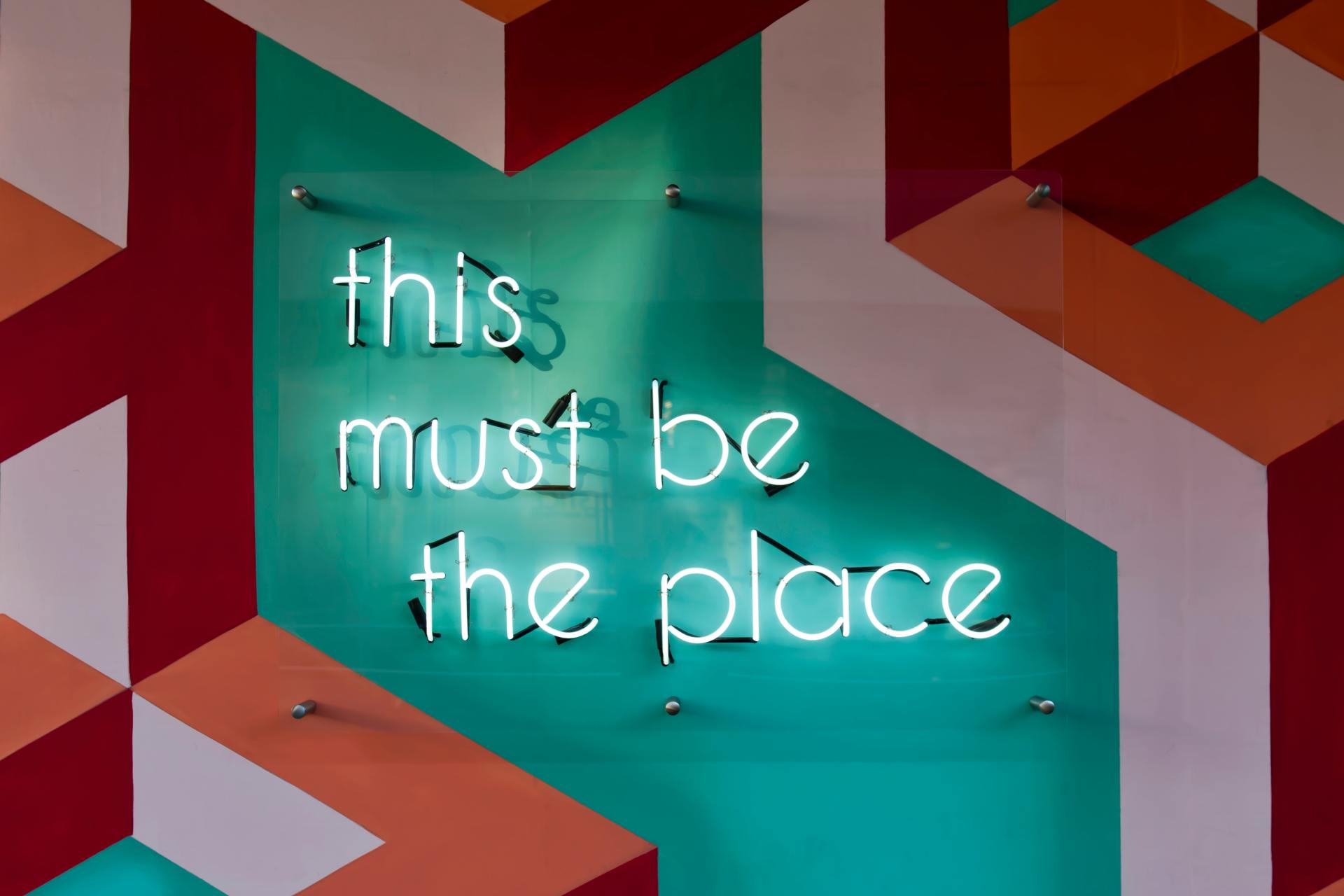 Image of a neon sign on a geometric color wall that says this must be the place